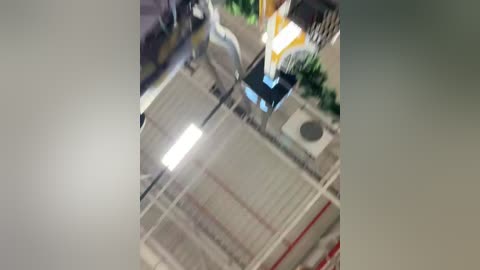 A blurry video of an indoor scene featuring a white-haired man in a striped shirt, standing in a room with green plants, a refrigerator, and a ceiling fan. The image is slightly out of focus.