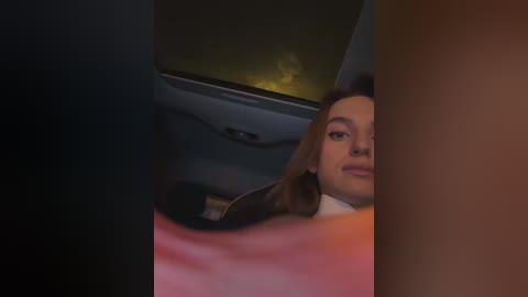 A video captures a woman in a dimly lit car, partially visible, with her head slightly tilted, wearing makeup, and a white top. The background shows a dark, blurry road and a yellowish light.