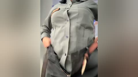 A video of a person in a green, military-style uniform, hands in pockets, with a visible patch on the left shoulder and a light-colored weapon holster on the right hip.