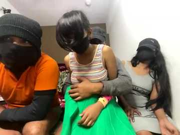 Video of three women in a room. One woman in orange, another in a striped top, and a third in a grey top. They're assisting a young girl in a green dress with a mask on.