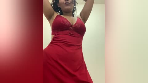 Video of a woman in a red lace lingerie dress with a plunging neckline, standing in a room with beige walls, her arms raised, and her wet hair partially covering her face.