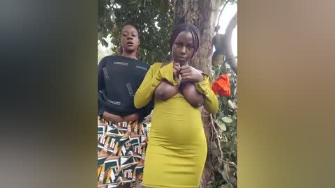 Video of two African women outdoors: one in a black shirt, the other in a yellow dress, pulling up to expose her large breasts.