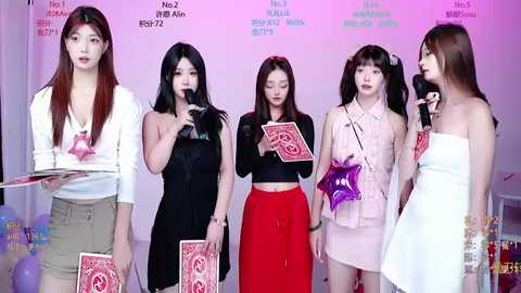 Video of five Asian women, three with long hair, two with short hair, in modern, colorful outfits, holding playing cards, in a casual indoor setting.