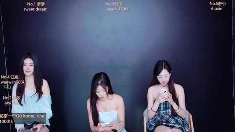 Media: Video of three young East Asian women, seated in a dark studio, wearing casual outfits, engaged in using smartphones, with text overlays in Chinese.