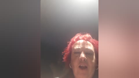 Video of a person with short red hair, eyes closed, mouth open in apparent ecstasy or pain, set against a gradient background of dark to light gray.