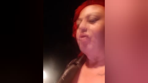 Video of a person with red hair, wearing a black shirt, singing into a microphone against a dark background.