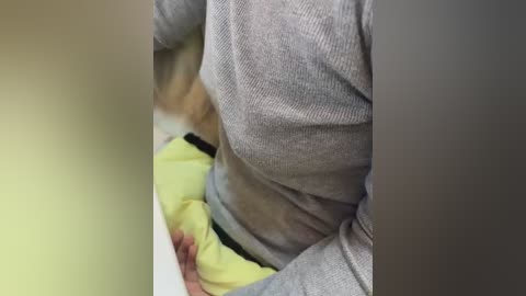 A close-up video of a person wearing a gray ribbed sweater over a yellow shirt, with the focus on their torso and lower face. The background is blurred.