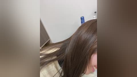 A video of a woman with straight, dark brown hair lying on a beige carpet in a dimly lit room. A blue shampoo bottle is partially visible in the background.