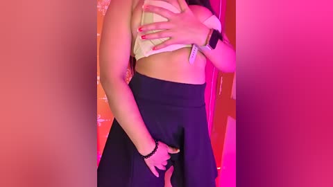 Media: Video of a woman with fair skin, wearing a beige bra, black pants, and a black bracelet, standing in a brightly lit room with red and pink hues.