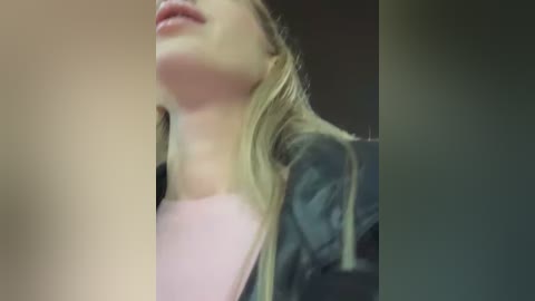 A blurred close-up video of a young woman with long blonde hair, wearing a pink top and a black jacket, looking up with her mouth slightly open.