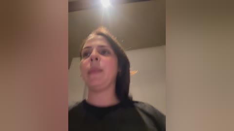 Media: Video of a Caucasian woman with long brown hair, wearing a black shirt, making an exaggerated face, taken indoors with soft lighting.