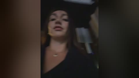Video of a young woman with fair skin, dark hair, and a black graduation cap, smiling slightly. She wears a black dress and a gold necklace. The background is blurred.
