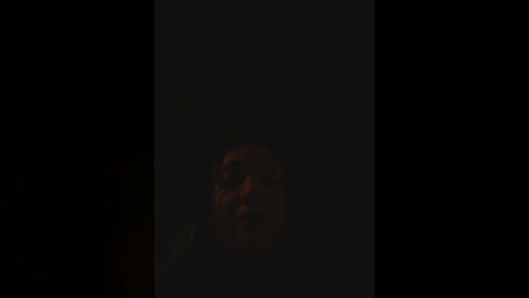 A dimly lit, shadowy video of a middle-aged man with a serious expression, his face partially obscured by darkness, creating a moody and mysterious atmosphere.
