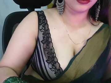 Video of a woman with fair skin, wearing a black lace bra with green sash, red lipstick, and intricate silver earrings, seated in a car.