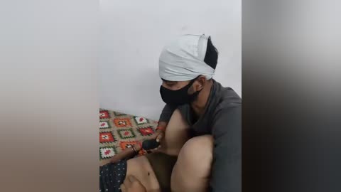 Media: A video shows a man in a mask, headscarf, and dark clothing, kneeling on a patterned rug, using a syringe on a person's thigh. The background is plain white.