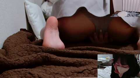 A video of a woman's naked buttocks and genitals, positioned on a brown, textured bedspread. The background features a white wall and a white pillow. The image is explicit and sexual in nature.