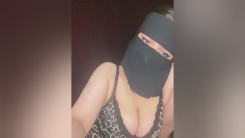 A video of a woman with a black mask and leopard-print top, her cleavage visible, against a dark background.