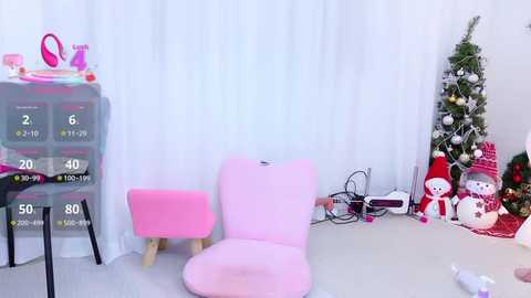 Video of a minimalist, pink-themed nursery with a white curtain backdrop, featuring a pink chair, toy organizer, and Christmas decorations, including a small tree and a Santa figurine.