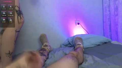 A video of a person lying on a bed, wearing beige socks, with a blue and purple light glowing under the sheets, highlighting the legs.