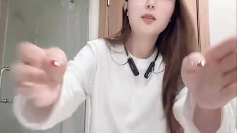Video of an Asian woman with long brown hair, wearing a white sweater, headphones, and looking down with a neutral expression.