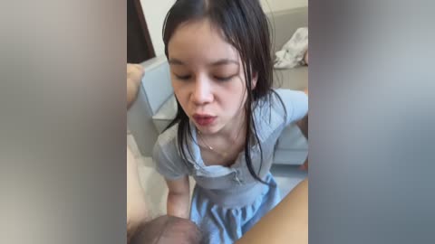 A video shows an East Asian woman with wet, dark hair, wearing a light blue shirt, performing oral sex on a man in a hospital setting.