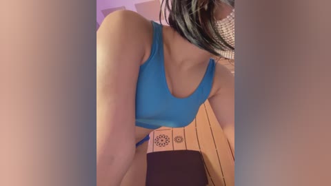 A video of a woman in a blue sports bra, seated on a wooden stool with a black and white pattern, partially obscured by a soft, blurred background.