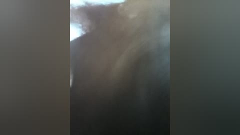 A blurred video of a person with dark, curly hair partially obscured by dense smoke, likely from a fire, creating a hazy, dark atmosphere. The person's facial features are indistinct.