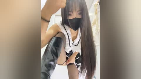 A video of an Asian woman in a black mask, white shirt, and black leather boots, crouching, viewed from above.