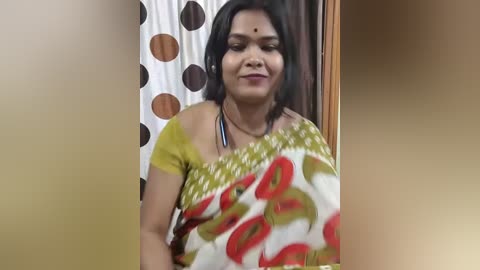 Media: A video of an Indian woman with medium-dark skin, wearing a colorful saree, standing indoors near a polka-dot curtain.
