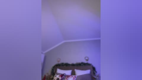A video of a dimly lit room with a ceiling corner showing a decorative wreath, featuring white pillows, and a faint purple hue.