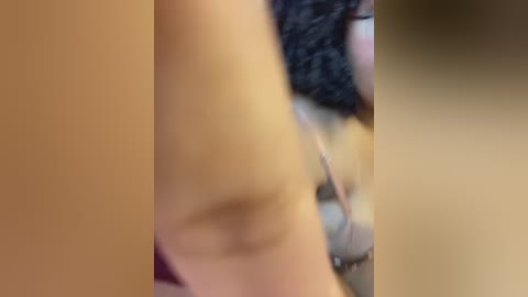 Video of a close-up of a person's arm with a tattoo on the forearm, blurred background, brown skin, and a black hair bun.