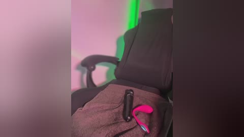 Media: A video showing a person's legs and arm in a black gaming chair with a pink and black controller, illuminated by green and pink light.