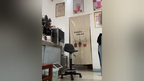 Video of a compact, well-organized office space with a black chair, a small desk, and a beige door adorned with red and white signs. The room features white walls and framed posters.