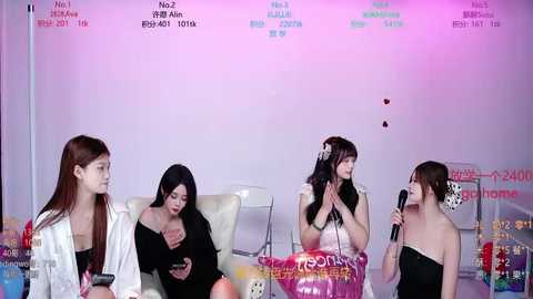 Video of four young Asian women with different hair colors and styles, sitting in a studio, holding microphones, wearing casual outfits, with colorful banners and text in the background.