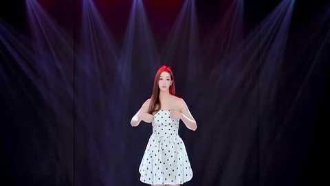 Video of a young woman with long red hair, wearing a strapless white dress with black polka dots, standing on stage under dramatic purple and red stage lights.