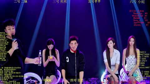 Video of five Asian performers on stage, dressed in casual, colorful attire, under bright stage lights, with a digital screen displaying text in the background.