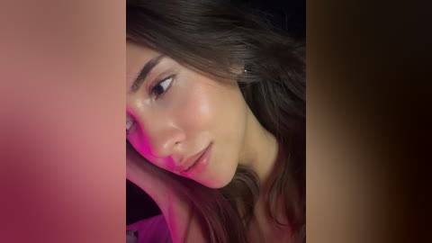 Video of a young woman with long, wavy brown hair, fair skin, and a serene expression, partially obscured by a pink and purple gradient background.