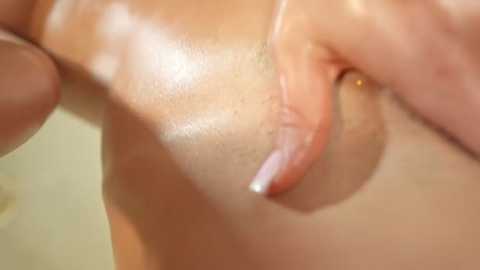 A close-up video of a woman's hand gently spreading oil on her bare, glistening breast, showcasing smooth skin and a natural, intimate setting.