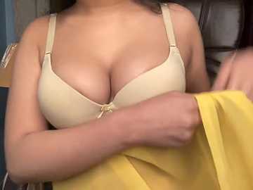 Video of a woman with medium skin tone, wearing a beige bra and yellow shirt, arms crossed over chest.
