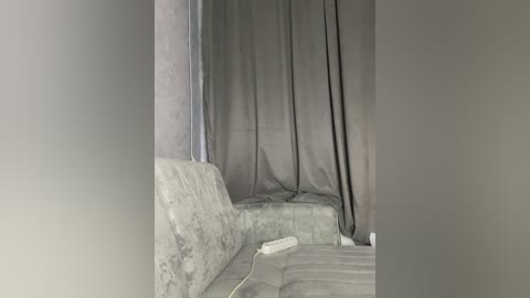 A video of a dimly lit room with a gray, patterned sofa, a white gaming controller on the armrest, and a black curtain partially covering the background. The room appears to be in a state of disarray.