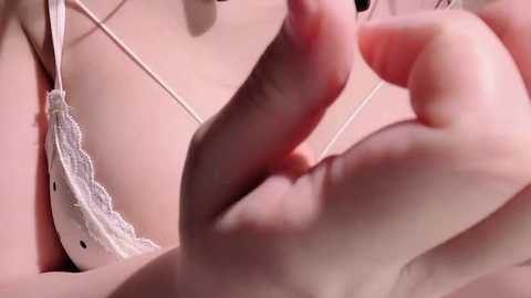 Video of a close-up of a woman's hand touching a white lace bra strap, set against a blurred, pale pink background.