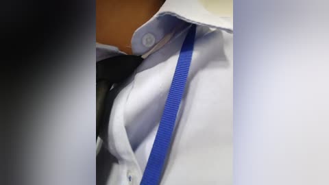 Video of a white dress shirt with a blue stripe on the collar, partially buttoned up, and a black tie hanging loosely.