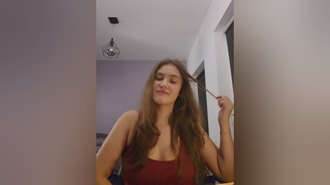 Media: Video of a young woman with long brown hair, wearing a red tank top, standing in a dimly lit hallway, holding a hairbrush.