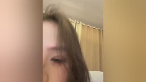 A blurred video shows a woman with long brown hair partially covering her face, standing in a beige-walled bathroom with a shower curtain.