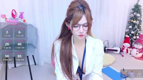 A video of a young Asian woman with long brown hair, wearing glasses, a white lab coat, and a black bra, seated in a brightly lit room with a Christmas tree and medical equipment.