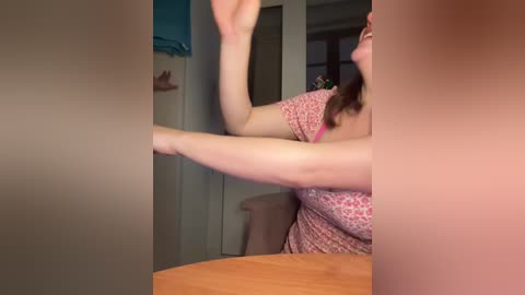 Video of a fair-skinned woman with medium-length brown hair, wearing a pink leopard print top, caught mid-action, arms raised, in a beige-tiled bathroom.