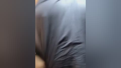 A close-up video of a person's back, wearing a dark gray, wrinkled, possibly plastic-like material, obscuring the face and upper body, with indistinct surroundings.