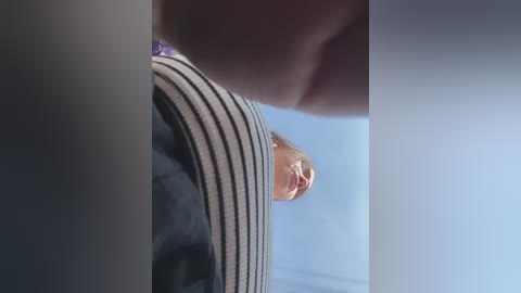 A close-up video of a woman's face and shoulder, wearing a striped shirt, with her head tilted to the side, in a dimly lit room.