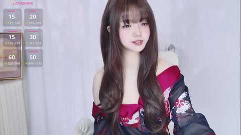 Video of a young Asian woman with long, straight brown hair, wearing a red kimono with floral patterns, standing against a white curtain background.