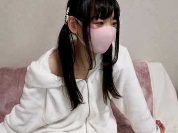 Media: Video of an Asian woman with long black hair in pigtails, wearing a white hoodie and pink mask, sitting on a pink couch against a beige wall.